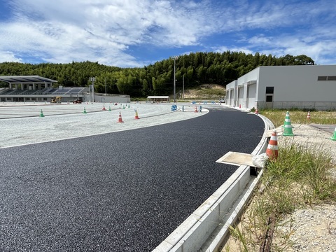 器具庫の前の左側にカーブした路盤工事が行われたアウトフィールドの上から基層工事が行われている様子の写真