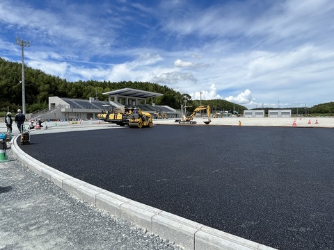 観覧スタンドに向かって右にカーブした路盤工事が行われたアウトフィールドの上から基層工事が行われている様子の写真