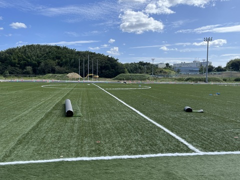 広大なフィールド内に人工芝が敷き詰められサッカーコートの外側と中央のラインが引かれている人工芝の敷設工事の様子写真