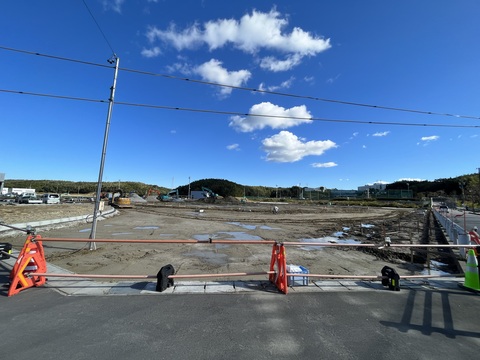交流広場付近の工事用鋼板塀が撤去された歩道と敷地内の境目に、オレンジ色のバリケードが設置されている建設予定地の写真