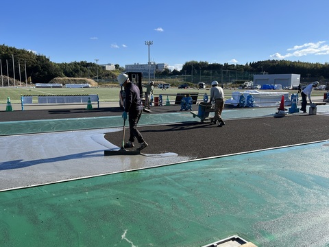 ヘルメットを被った作業員が、薄いグレー色のウレタンでトラック部分を舗装している写真