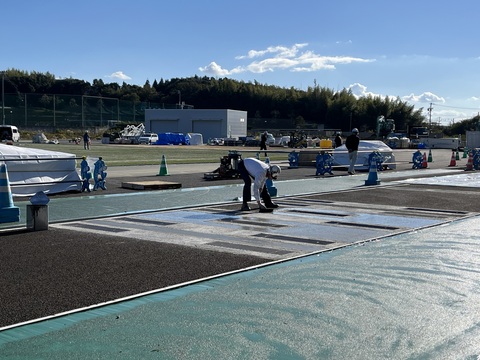 ヘルメットを被った作業員が上半身を屈めながら、トラック部分をウレタン舗装している工事の様子写真