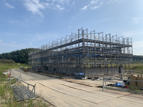 周囲に草が生えた陸上競技場器具庫の建設現場で足場が組み立てられている様子の写真