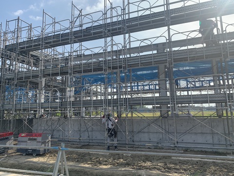 2名の作業員が、地上と2階部分に昇り陸上競技場器具庫の足場を組み立ている様子の写真