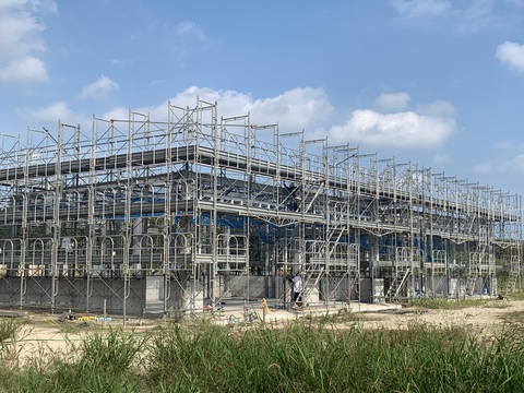 2名の作業員の方が2階部分と地上に分かれて、陸上競技場器具庫の建設現場の周りで足場を組み立てている様子の写真