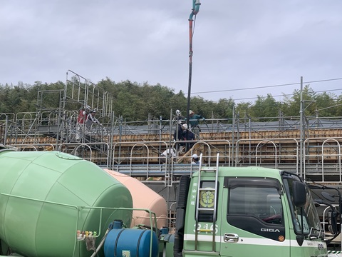 コンクリートポンプ車から延びてきたブームを使い、4名の作業員が陸上競技場観覧スタンド2階部分でコンクリート打設工事を行っている様子の写真