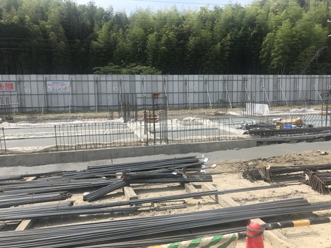 コンクリート打設工事が行われている陸上競技場観覧スタンド1階床部分の周囲に、長さごとに揃えられた鉄筋が地面に置かれている工事の様子写真