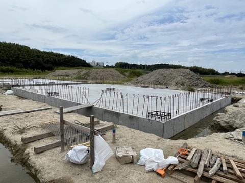 土が山積みにされ、周囲に資材や道具が置かれた陸上競技場器具庫の建設現場で、床部分のコンクリート打設工事が行われている様子の写真
