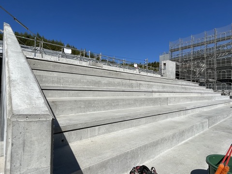 足場が組まれネットで覆われた陸上競技場観覧スタンドの左側の観覧席部分に段床版が設置された写真