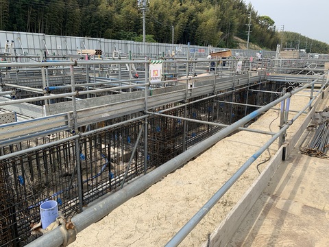 建設予定地の陸上競技場観覧スタンドに鉄筋が組まれ、ヘルメットを被った作業者が配筋工事を行っている様子の写真