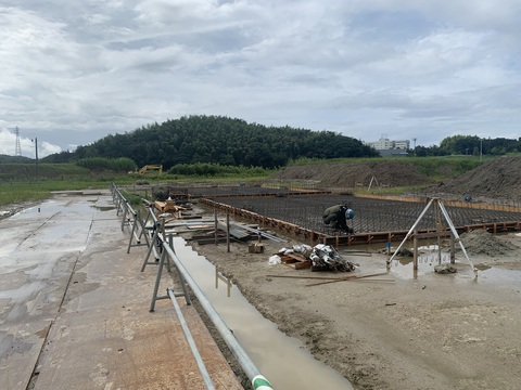 陸上競技場器具庫の建設現場でヘルメットを被った作業員が床部分の工事を行っている様子の写真