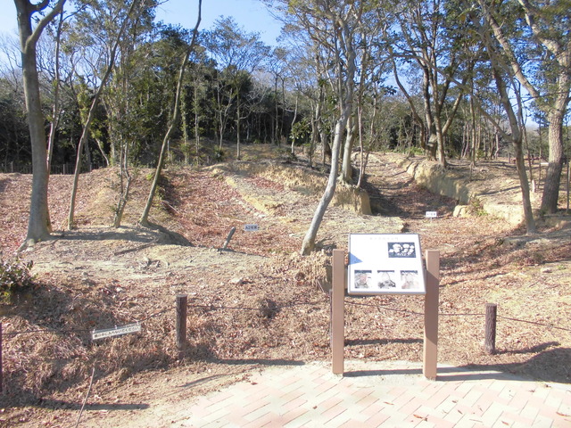 奥まで続く木々と古窯群が見える遊歩道に案内板がある風景写真