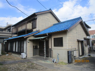 青色の瓦屋根で2階建のベランダがあり窓が多く設置された住宅の外観写真