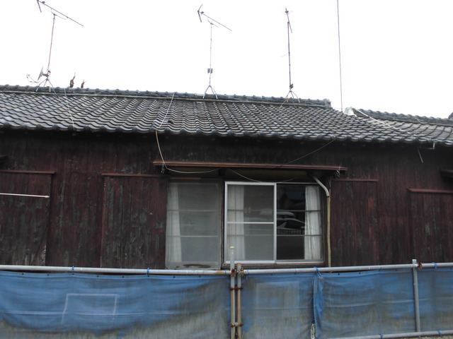 鉄筋やネットで囲ま間れた瓦屋根のこげ茶色の木造平屋建てで外壁写真