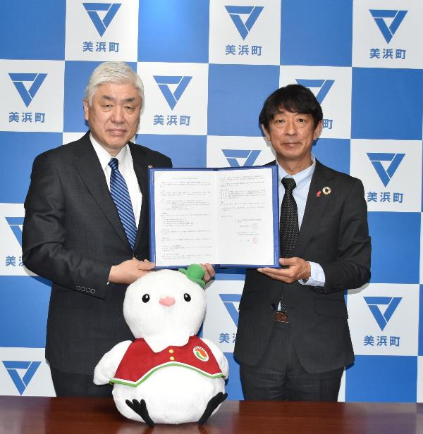 美浜町のバックボードの前に立ち、伊藤会長と八谷副町長が一緒に協定書を持っている写真