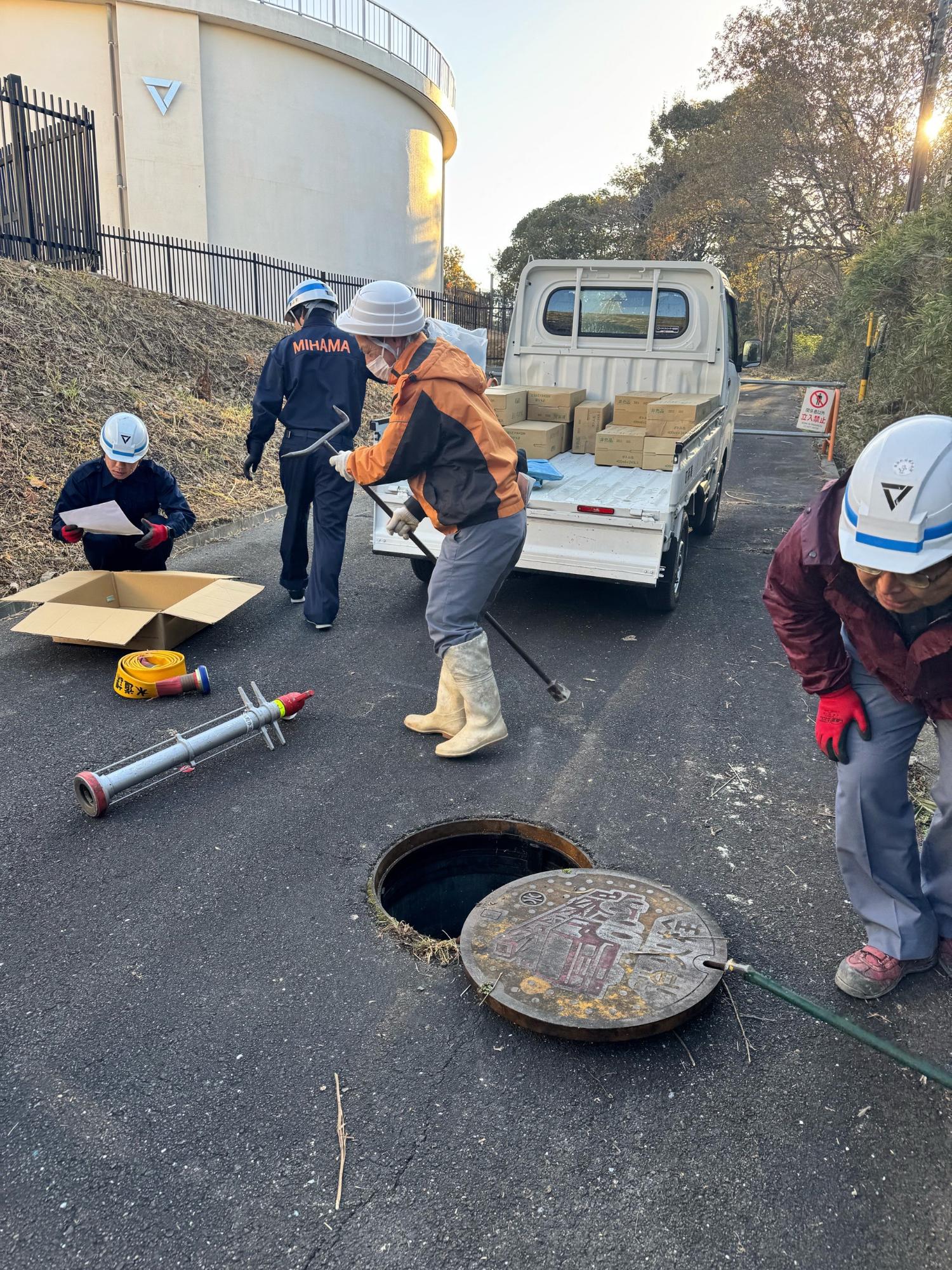 ヘルメットを被り作業着を着た職員の方が、道路にあるマンホールを道具を使って開けている写真
