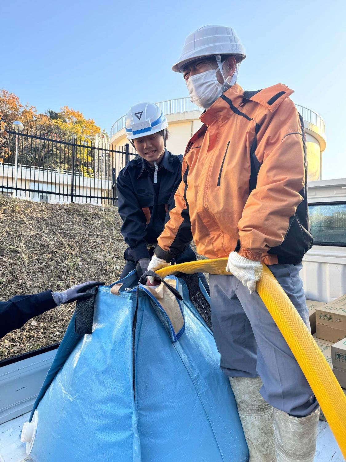 黄色いホースを水色の簡易給水槽に繋ぎ給水を行っている様子の写真