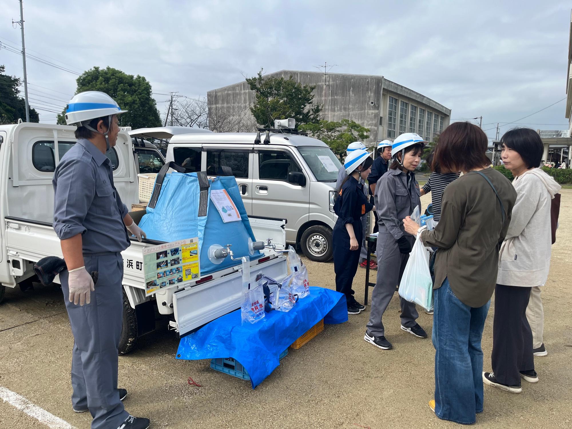 軽トラックの荷台部分に積まれた簡易給水槽から給水袋へ水を入れている写真