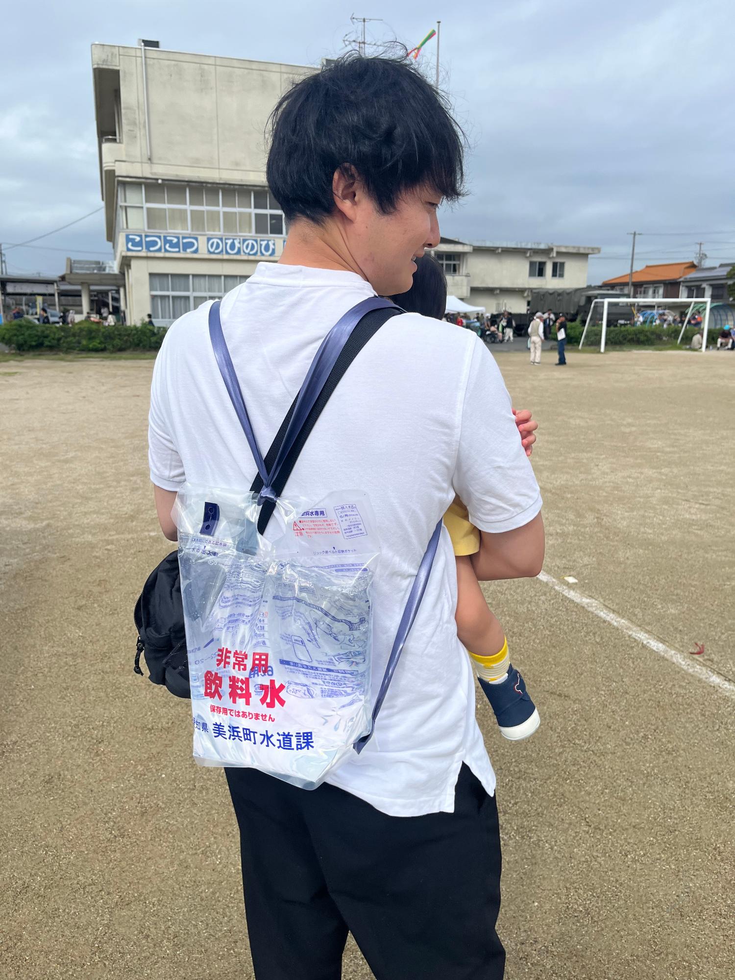 背負い式給水袋を背負っている男性が、子供を抱っこしている写真