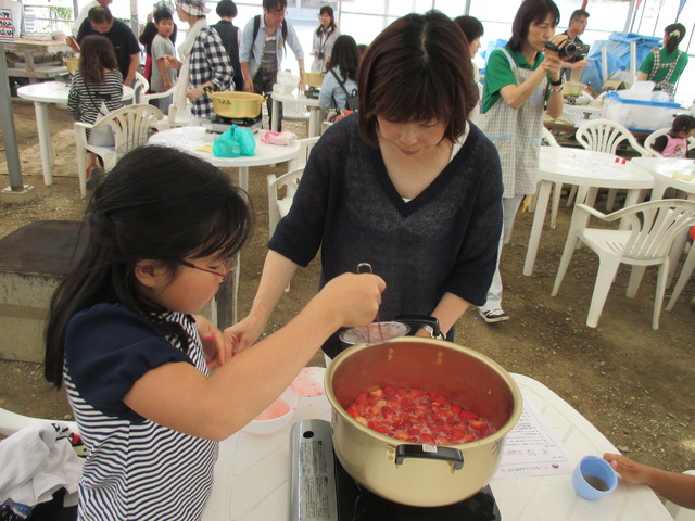 網杓子を使って鍋の灰汁をすくっている女の子と横に立って見守るは母親の写真