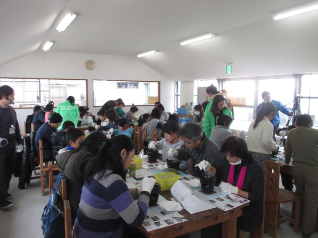 固形燃料が入った小さなコンロの上に乗っている鍋を、参加者たちが真剣にスプーンでかき混ぜている塩作り体験の様子写真