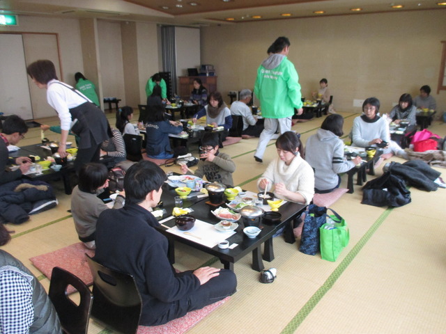 広い和室に等間隔に並べられた座卓に座り参加者たちが食事をしている写真