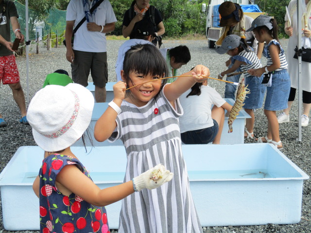 サクランボ柄のワンピースに白い帽子姿の女の子の横でグレーと白のストライプのワンピース姿の女の子が釣ったエビをうれしそうに見せている写真