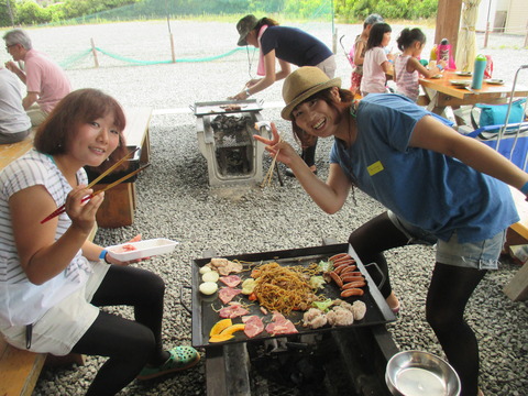 鉄板の上で焼きそばや肉や野菜を焼いてピースサインをしている2人の女性の写真