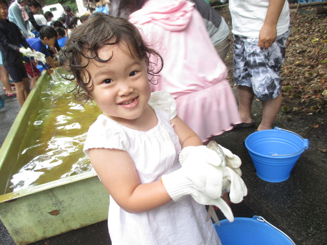軍手を付け、魚を捕まえた女の子が嬉しそうにカメラに笑顔を見せている写真