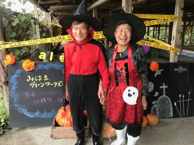 ハロウィーンの仮装で黒と赤の衣装を身にまとい、とんがり帽子をかぶった冨谷夫妻が腕を組み笑顔で写っている写真