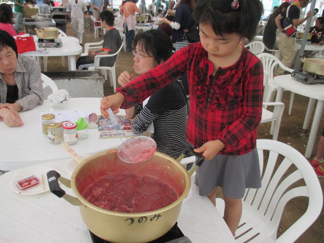 大きな鍋で煮詰めたイチゴの灰汁を網杓子ですくっている女の子の写真