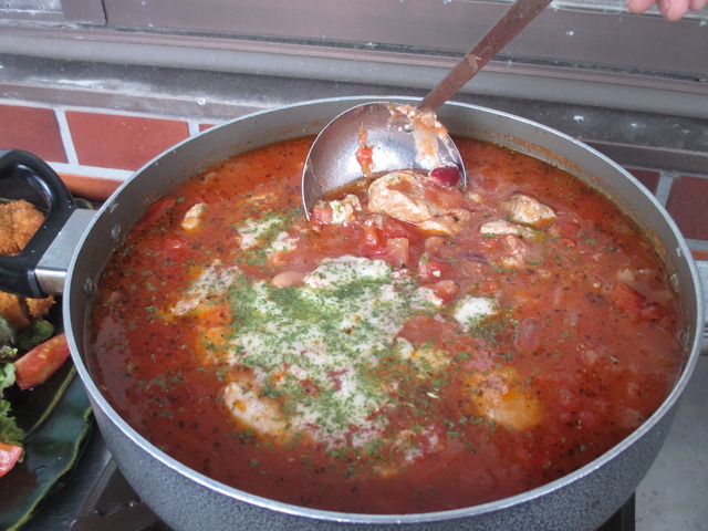 大きな鍋にいろいろな具材がはいっている煮込み料理をお玉でまぜている様子を写した写真