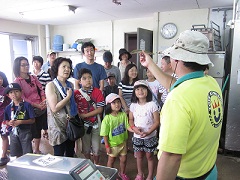 水族館のバックヤードに案内されて飼育員から説明を聞いている参加者の写真