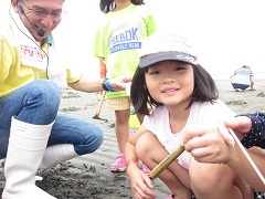 砂浜で取ったマテ貝を持っている笑顔の女の子の写真