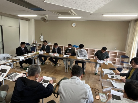 テーブルと椅子がロの字に設置され、関係者が集まり資料を手元に会議が行われている様子の写真