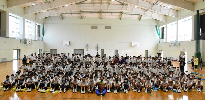 体育館で、磯部誠選手を中心に全校生徒の皆さんと記念撮影をしている写真
