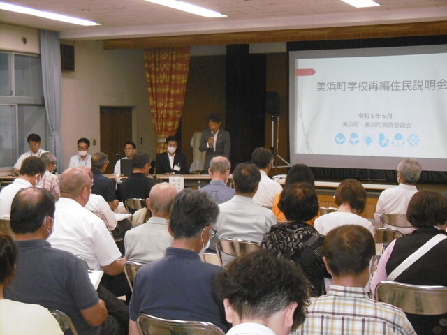前方に資料が映し出されたスクリーンが設置され、マイクを持ったスーツ姿の関係者の男性が、集まった多くの住民へ説明している様子を室内の後方から写した写真