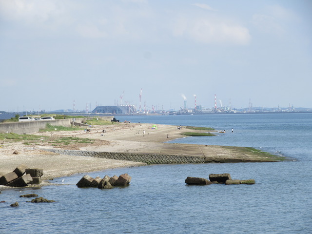 人が歩いている砂浜の一角に、傾斜をつけて海面の方へ伸びている滑走台が残っている写真