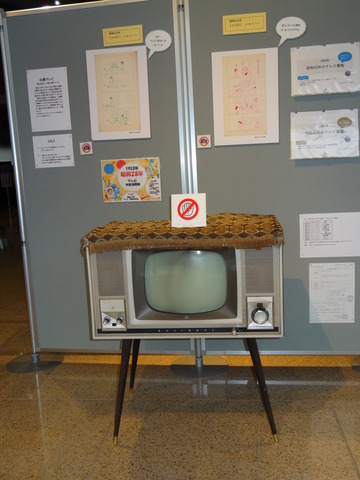 4つの足がついたブラウン管テレビや、イラストなどが貼られたパーテーションが一緒に展示されている写真