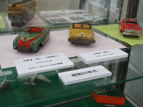 説明文とともに赤色や黄色、緑色など、カラフルな車のおもちゃが複数展示されている写真
