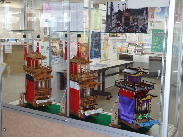 ショーケース内に赤色や紫色にデザインされた3台の布土山車が展示されている写真