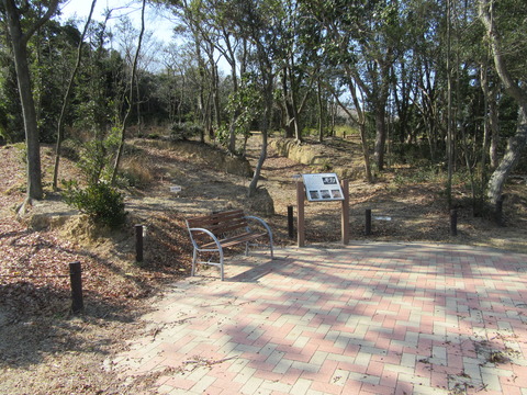 周囲に木々が生えている遊歩道の一角に、看板やベンチが設置されている写真