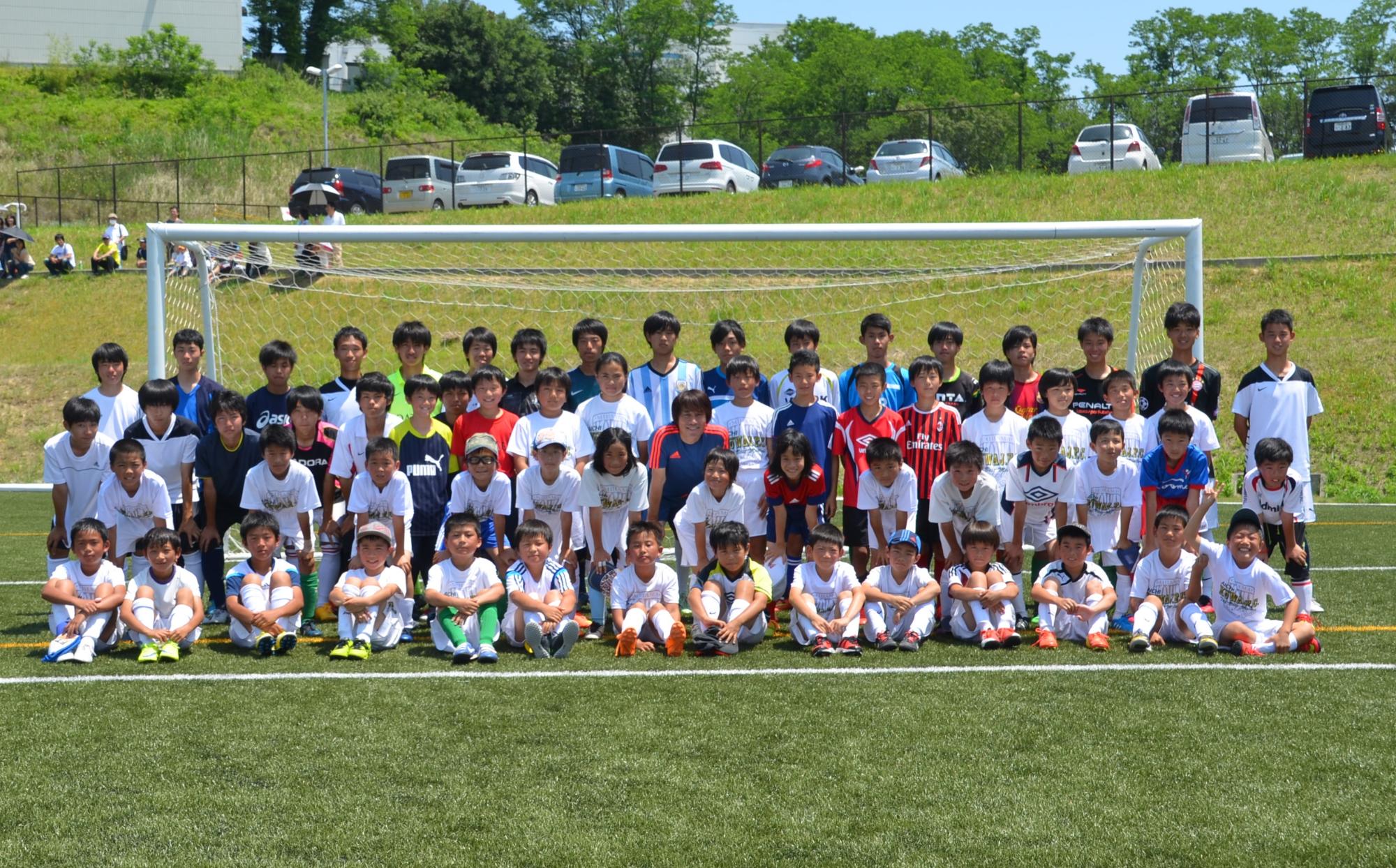 中西さんを中心にゴールポストの前でジュニアサッカー教室参加者の人達と記念撮影をしている写真
