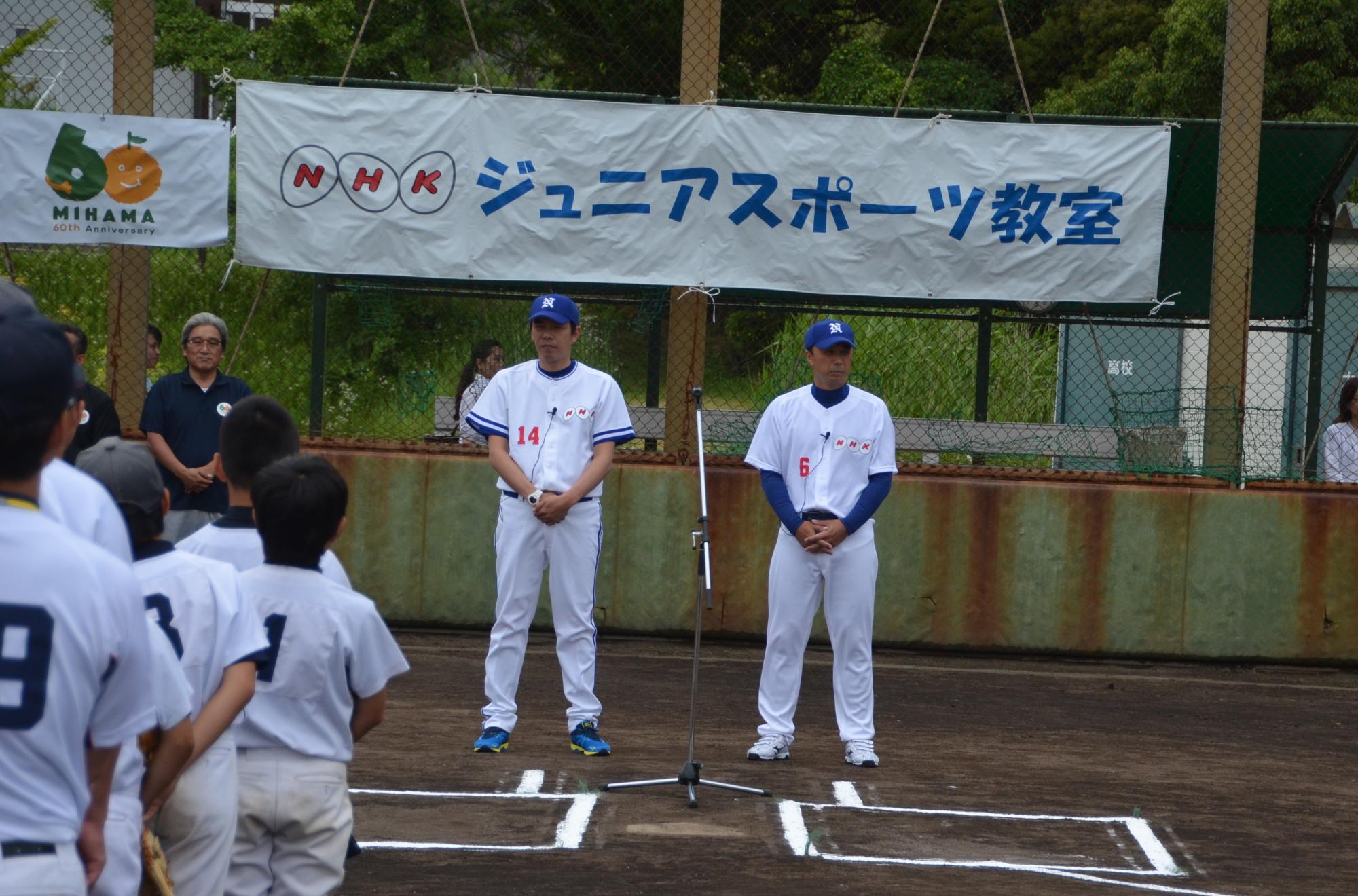 NHKジュニアスポーツ教室と書かれた幕が飾られた球場のホームベースの後ろにマイクが設置され今中慎二さんと宮本慎也さんが並んで立っている様子を写した写真