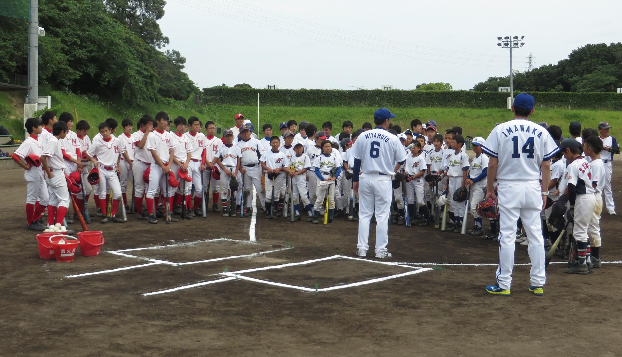 バットを持った子供達がホームベース付近に立つ今中慎二さんと宮本慎也さんの話を聞いている写真