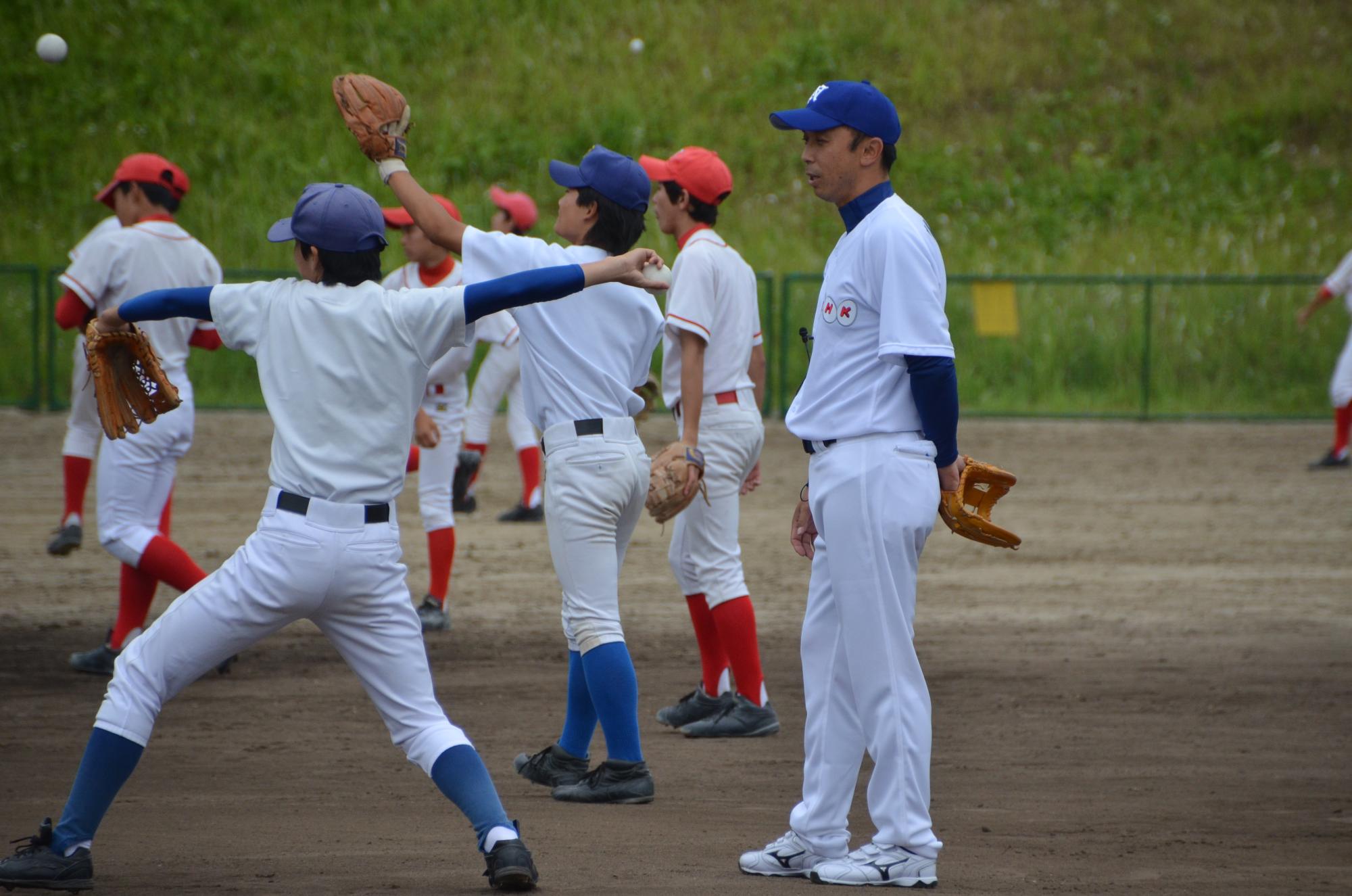 青い帽子にソックス、赤い帽子にソックスのユニフォームを着た子供達がキャッチボールをしている後ろから今中選手が指導している写真