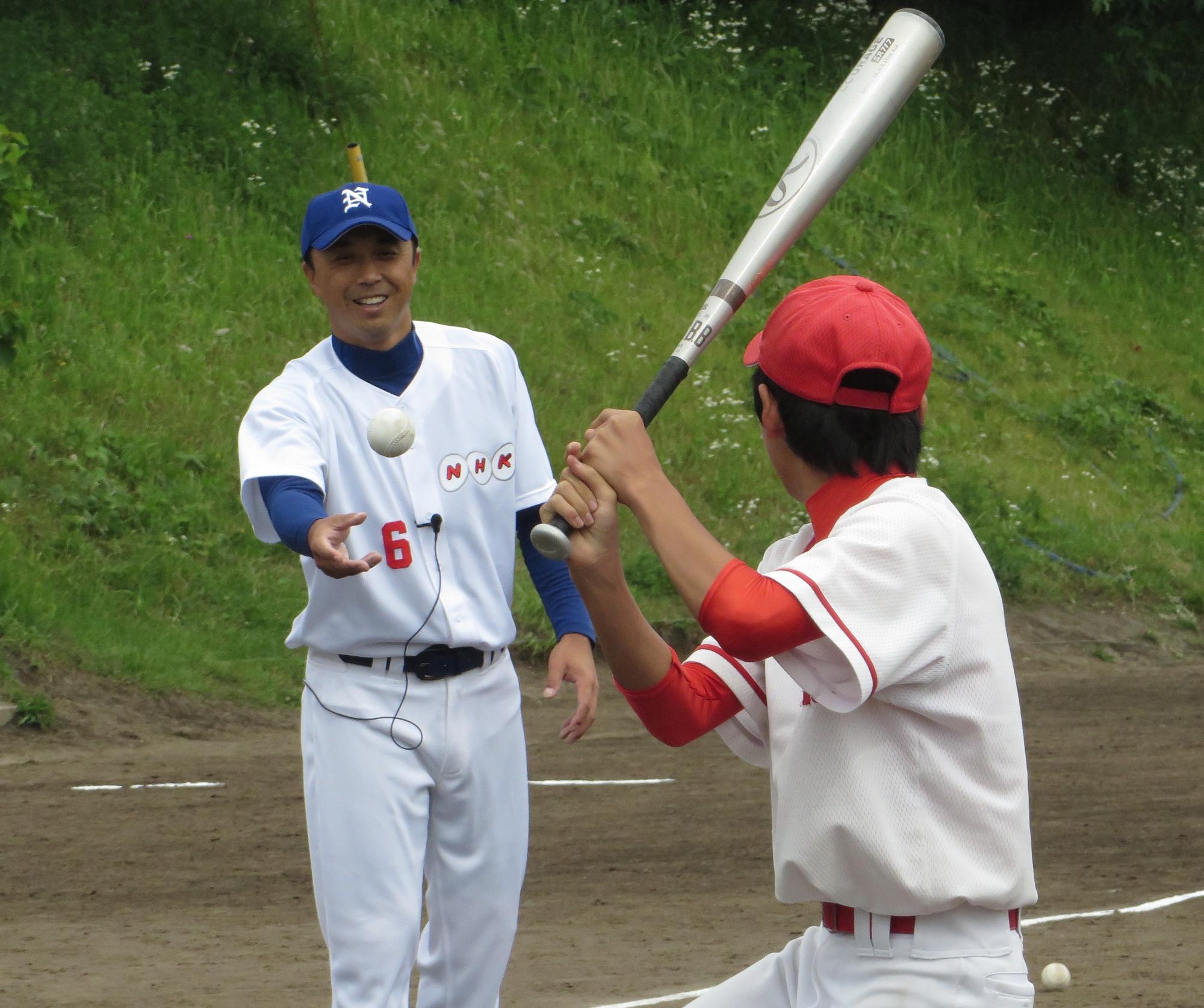 宮本選手が投げるボールを赤い帽子姿の中学生がバットで打とうとしている写真
