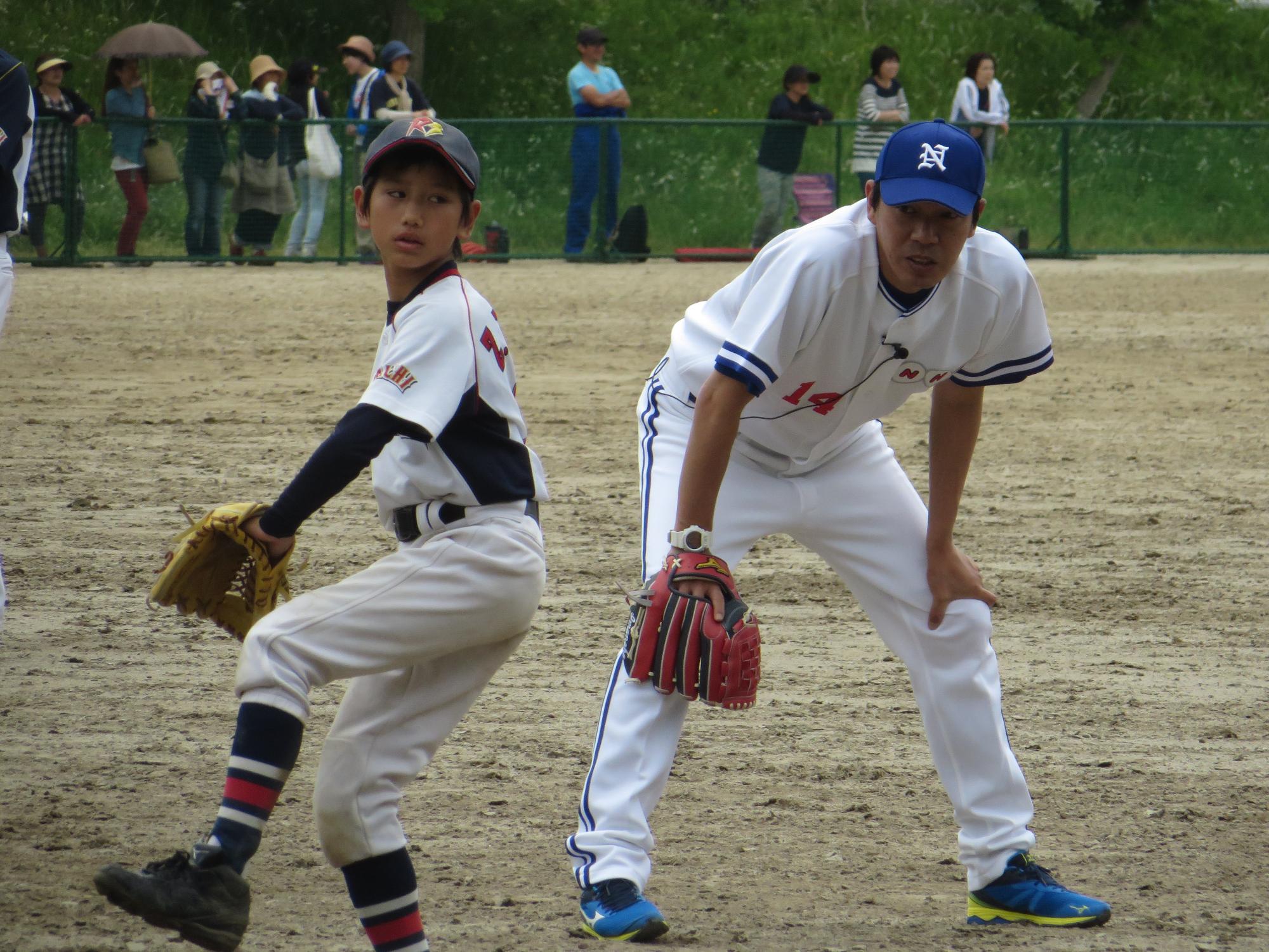 ピッチングをする小学生の男の子の横にグラブを持った今中選手が中腰でみている写真