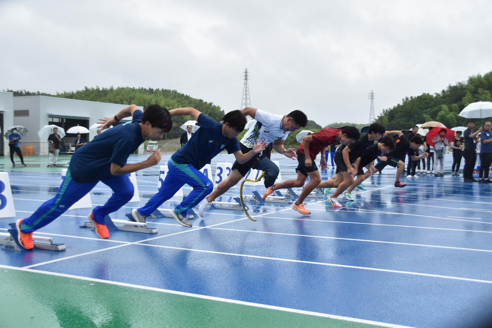 陸上競技の青いトラックの上で選手達が並び走り出すデモンストレーションの様子の写真