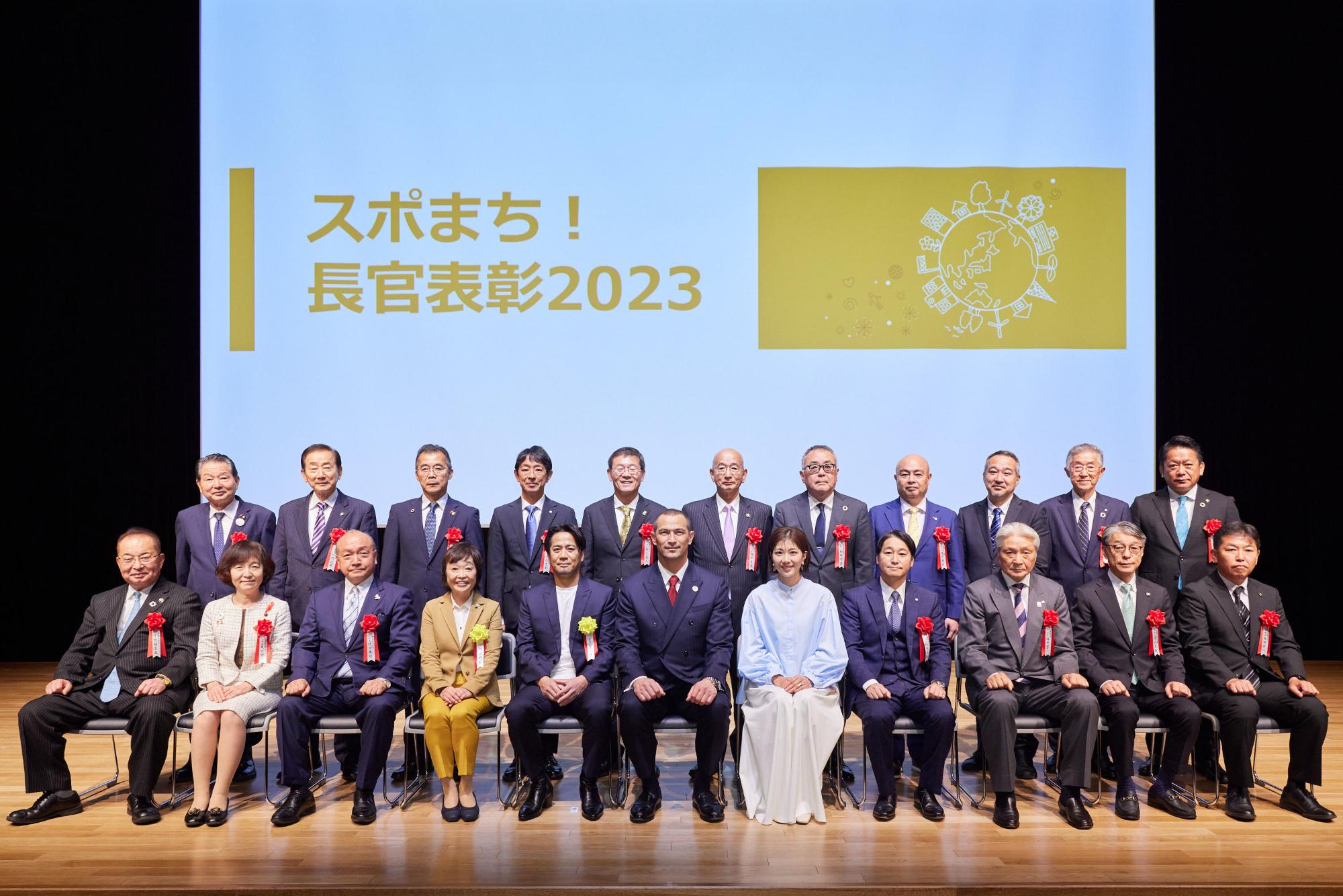 後ろのスクリーンに「スポまち！長官表彰2023」と書かれ、前列の方が座り後ろの列の関係者の方々が立って並んだ記念写真